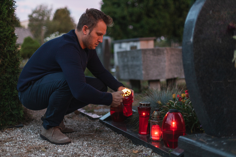 Mann zündet eine Kerze am Grab an.